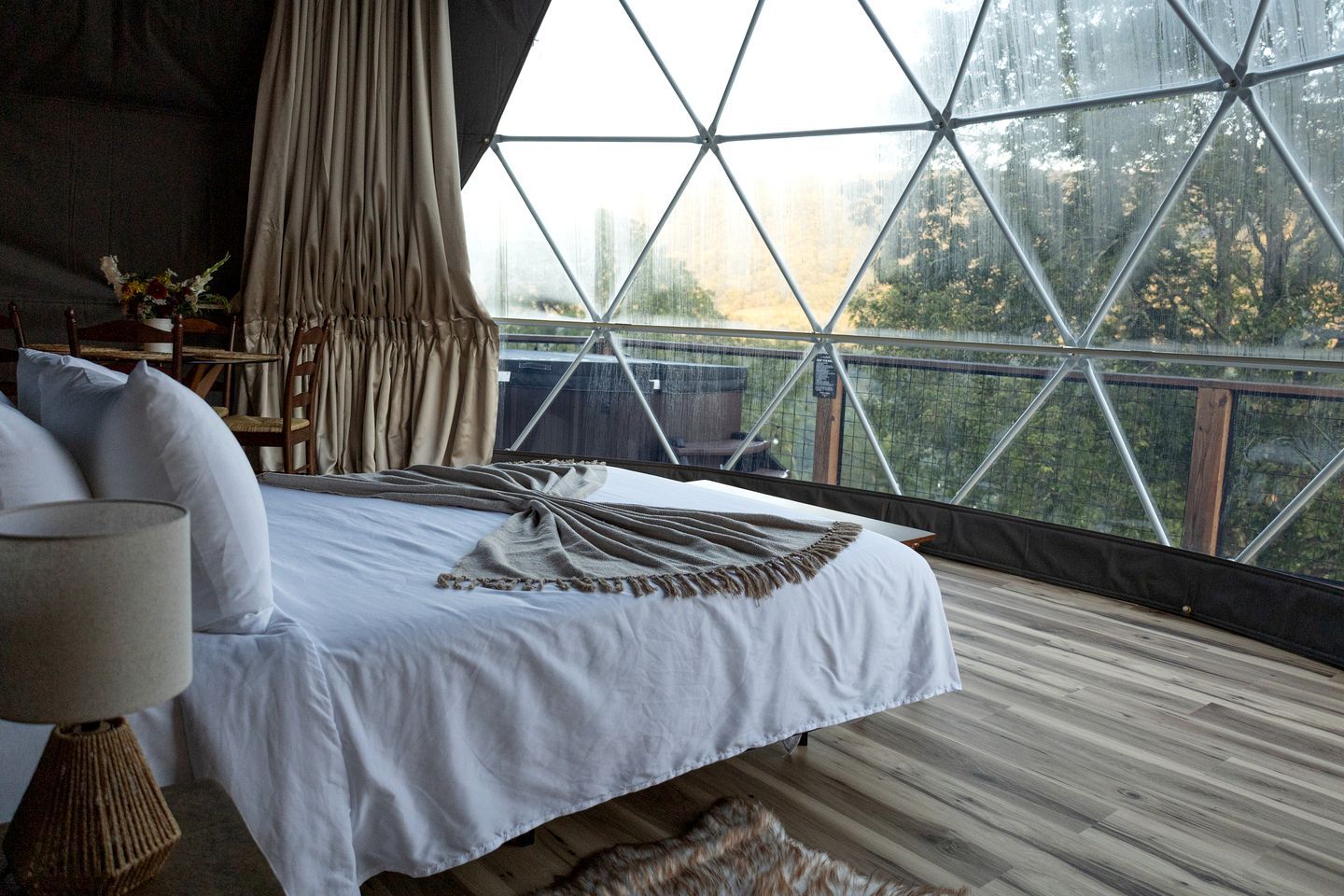 Un dormitorio con una cama grande, suelo de madera y vistas a través de un ventanal de diseño geométrico.