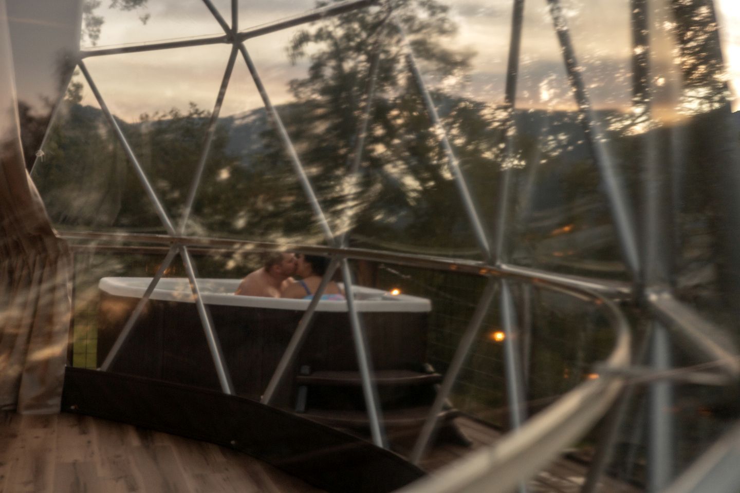 A glass-enclosed hot tub with a view of trees and mountains.