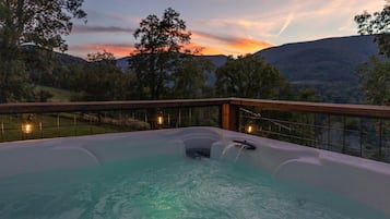 A hot tub with a view of a sunset and hills.