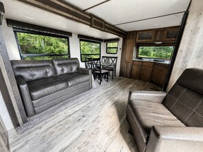 A compact RV interior with a sofa, dining table, chairs, and a kitchen area. - Spacious Rental Camper with Private Bathroom near Lake Champagne, Randolph, Vermont (Randolph)