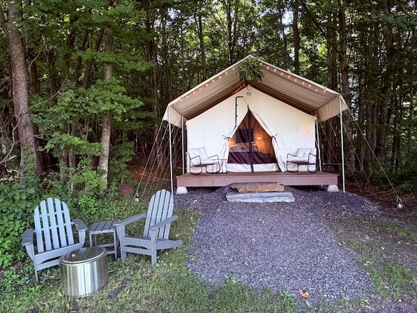 Una tenda con un letto e due sedie, immersa tra gli alberi.