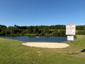 Segnale di avvertimento vicino a un lago, con cielo sereno e alberi sullo sfondo.