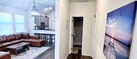 A hallway with a dining area, a living room with a brown leather sofa, and a painting on the wall.