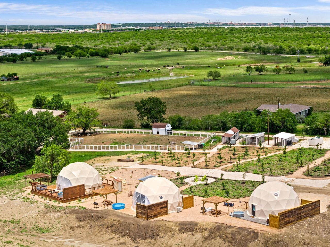 Ein ländliches Anwesen mit mehreren kuppelförmigen Gebäuden, einem umzäunten Bereich und Blick auf eine grüne Landschaft.