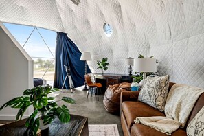 Ein modernes Interieur mit einem großen Fenster, einem Ledersofa, einem Schreibtisch mit Lampe und einem Stativ.