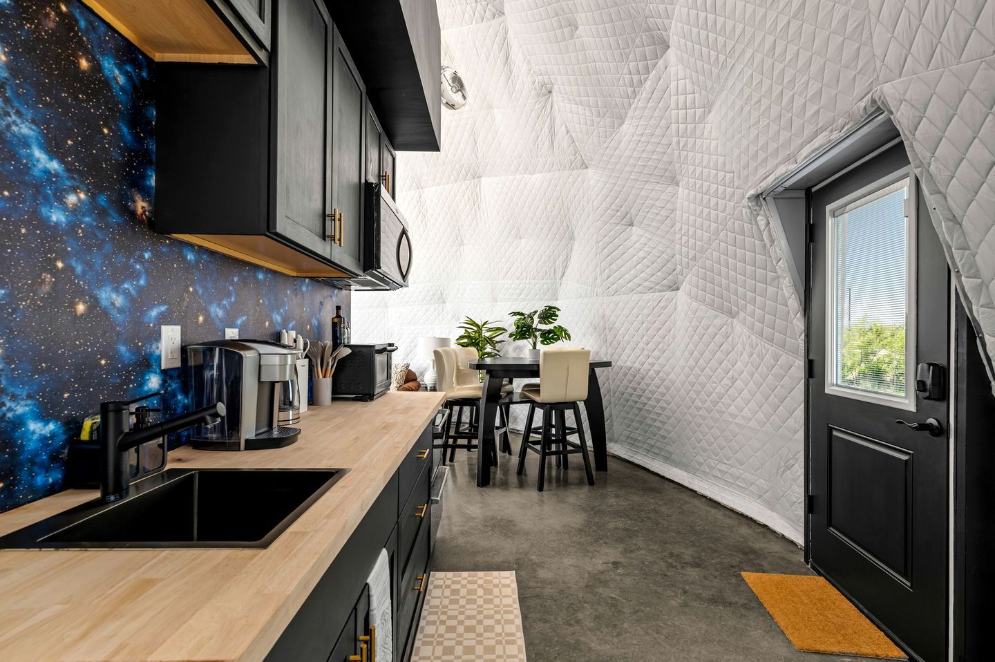 A compact kitchen with a galaxy-themed backsplash, a dining area with a table and chairs, and a door with a window.