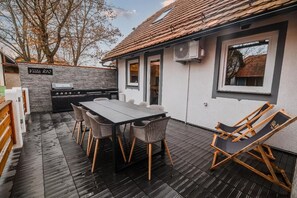 Eine Terrasse im Freien mit Esstisch, Stühlen, Grill und Liegestuhl.