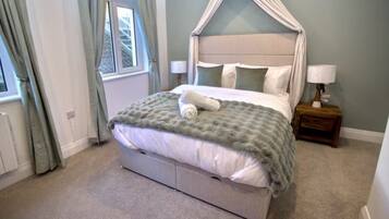 Un dormitorio con cama a dosel, una mesita de noche con lámpara y una ventana con cortinas.