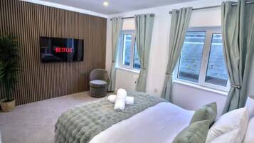 Una habitación de hotel con una cama, un televisor montado en la pared, una ventana con cortinas y una planta en maceta.
