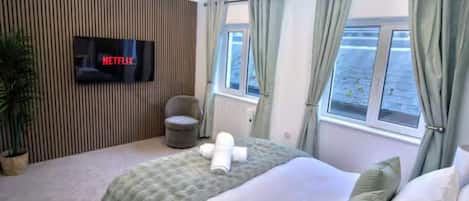 Una habitación de hotel con una cama, un televisor montado en la pared, una ventana con cortinas y una planta en maceta.