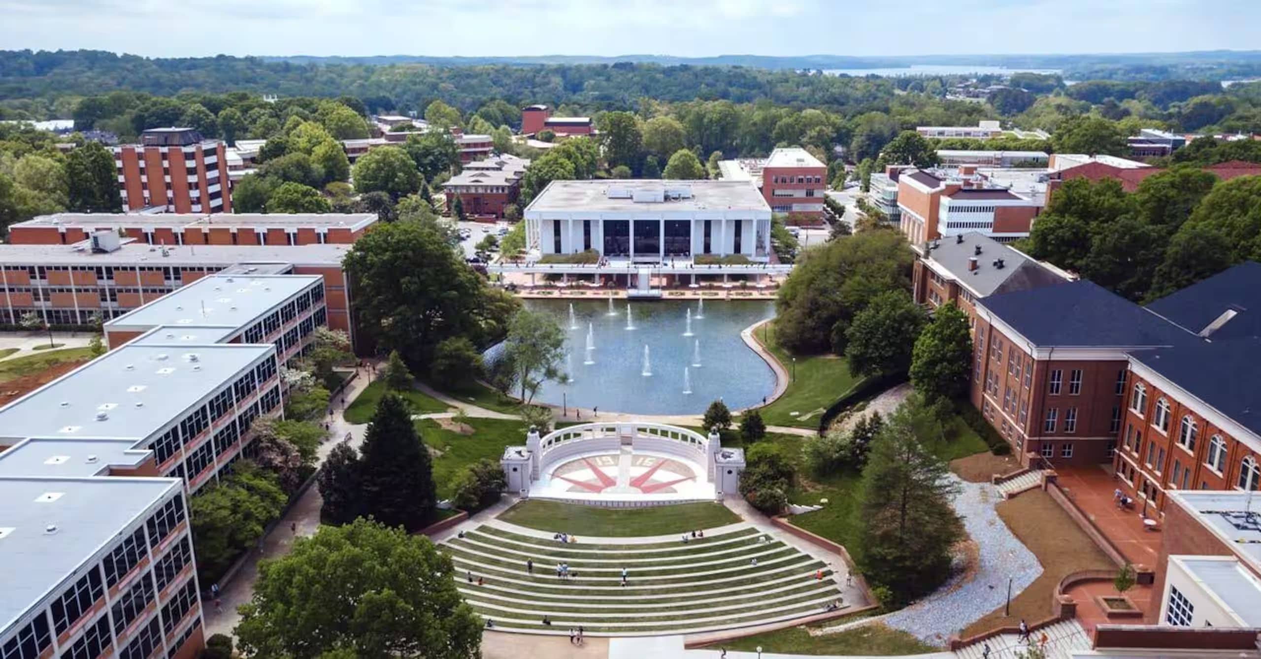 An aerial view of a university campus with a central courtyard, buildings, and a large body of water.