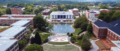 An aerial view of a university campus with a central courtyard, buildings, and a large body of water.