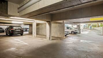 An underground parking garage with concrete pillars, marked parking spaces, and a few cars parked.