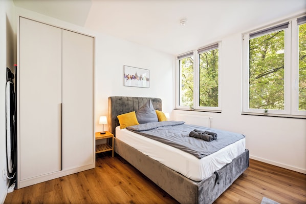 A bedroom with a bed, bedside table, lamp, and a cityscape picture on the wall. - Modern apartment in the heart of Wiesbaden. Ideal for temporary housing. (Wiesbaden)