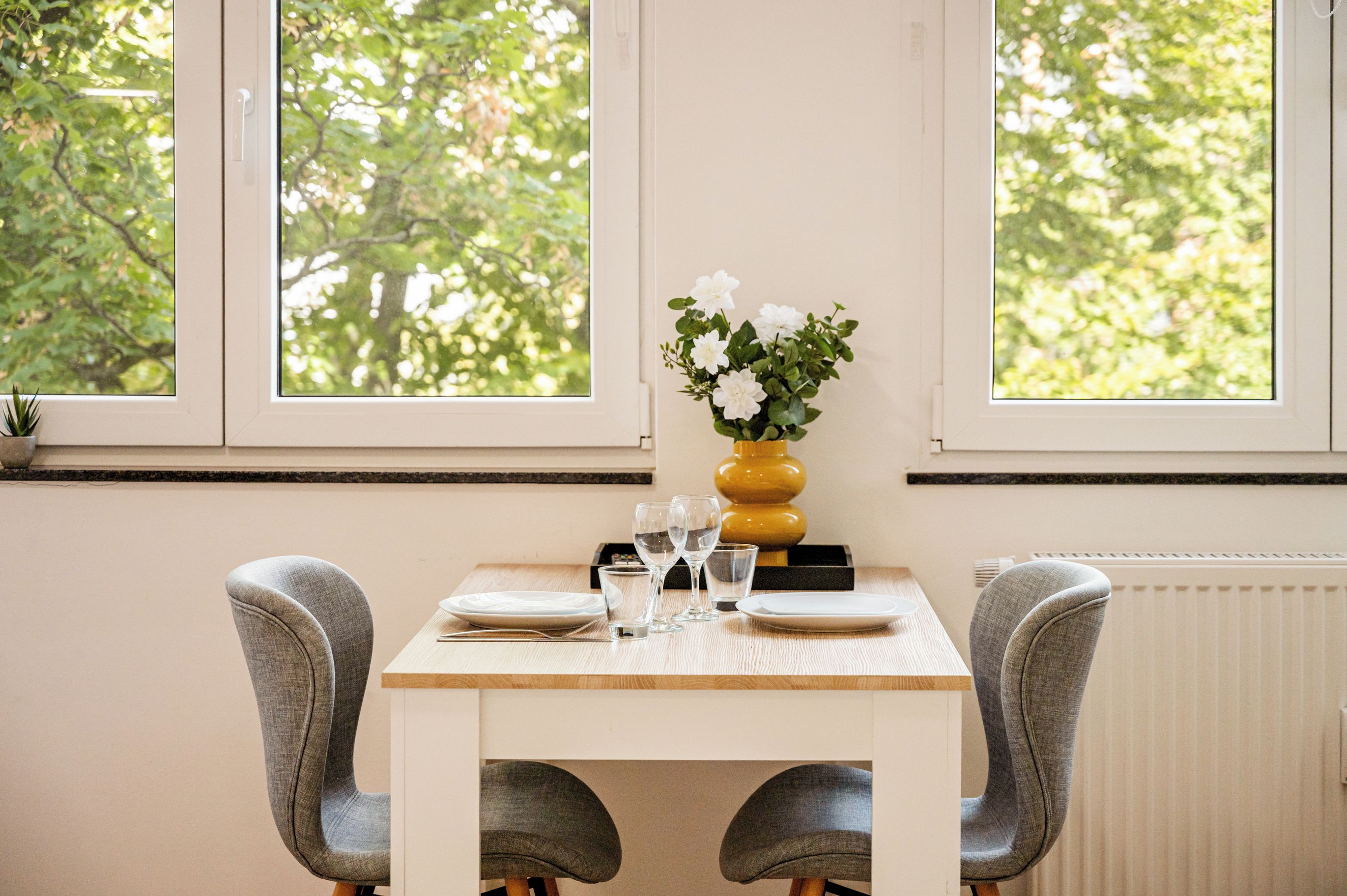 A dining table with chairs, a vase with flowers, and glasses.