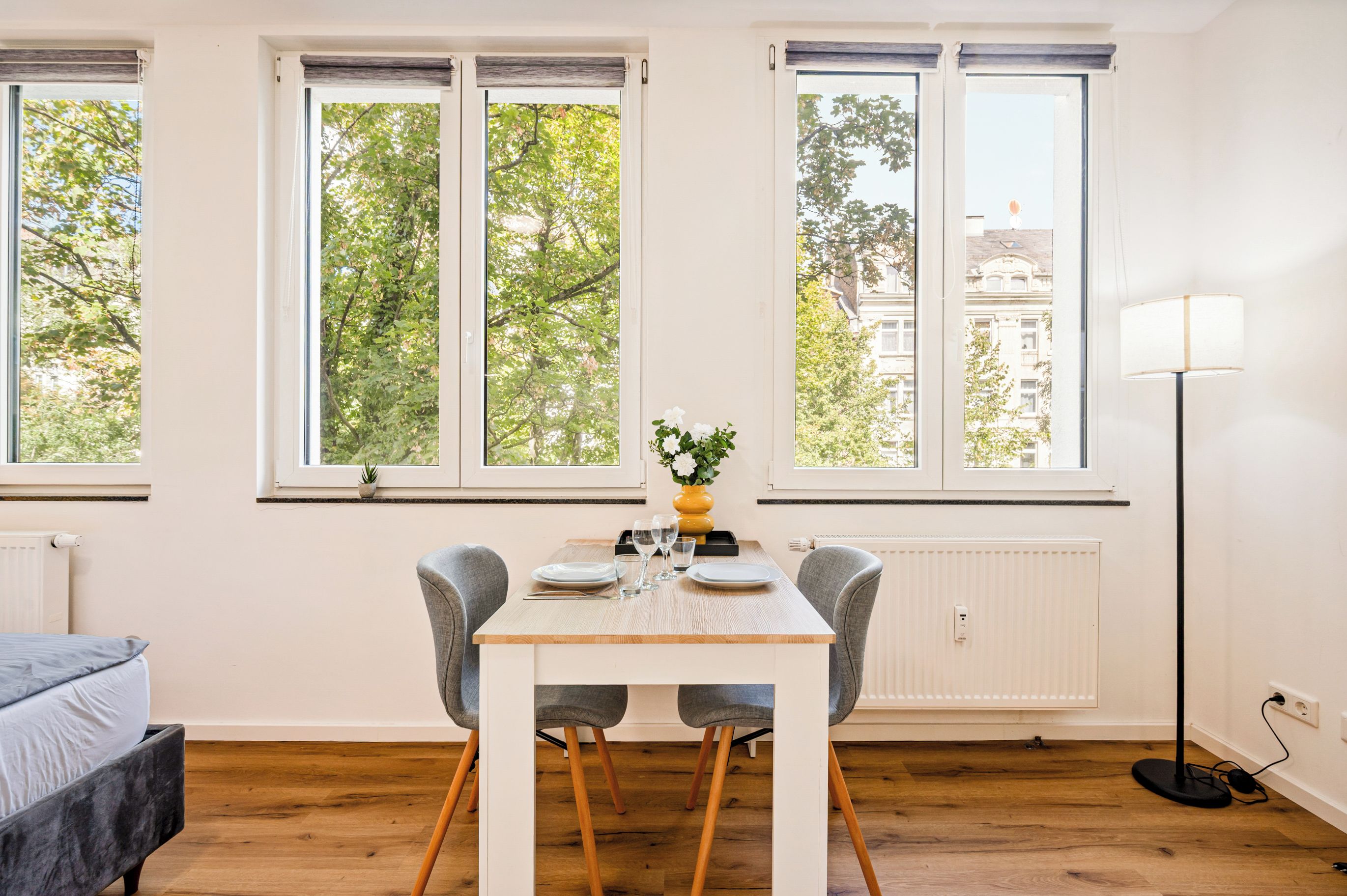 A dining area with a table set for two, two chairs, a vase with flowers, and a lamp.