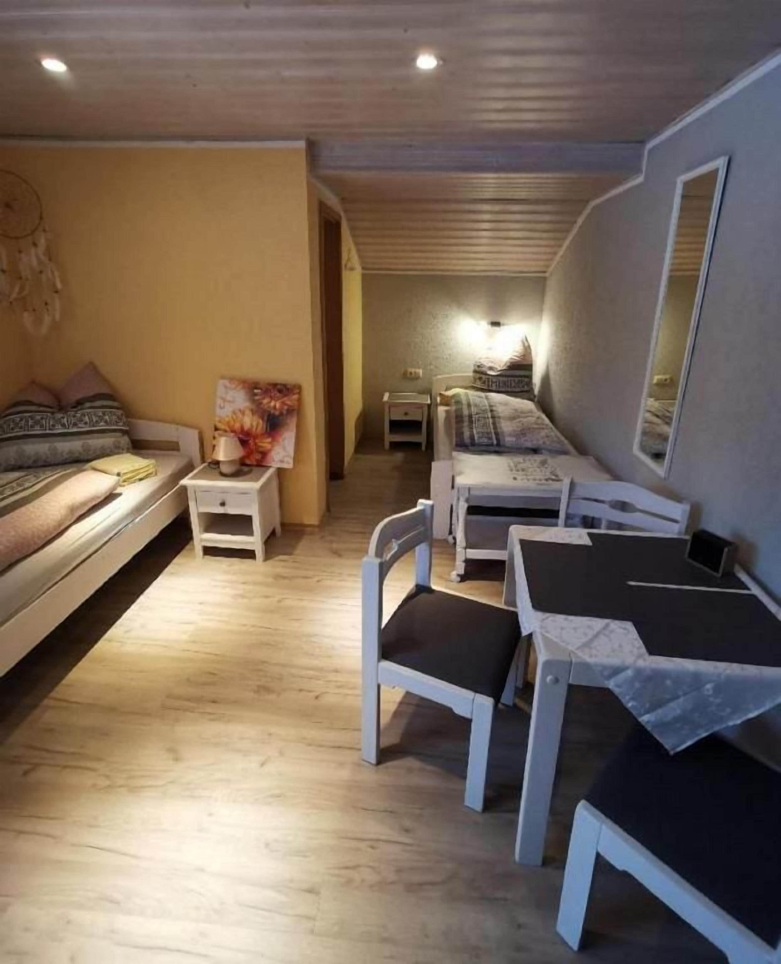 Une pièce de taille modeste, comprenant un lit, un bureau et une chaise. On y trouve une petite table avec une lampe, ainsi qu’un miroir fixé au mur.