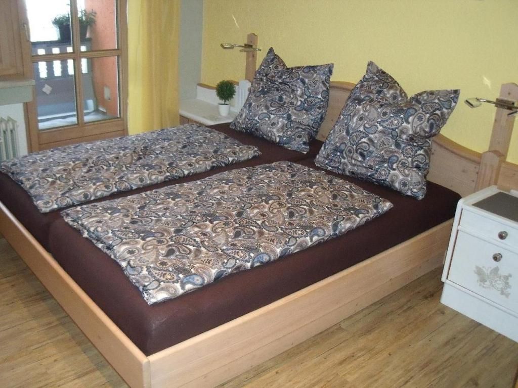 Una cama doble con ropa de cama y almohadas estampadas, un cabecero de madera, una mesita de noche con una lámpara y una ventana con vistas.