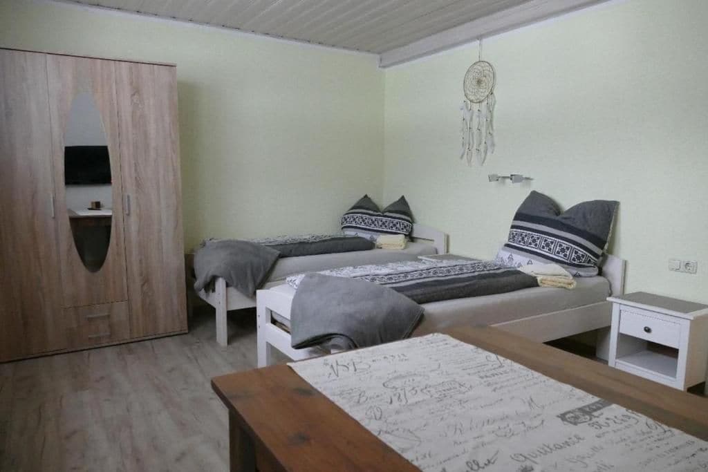 A bedroom with two beds, a wardrobe, a bedside table, and a dreamcatcher on the wall.