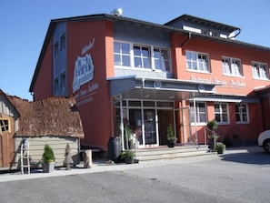 En bygning med rød facade, et skilt der siger 'Restaurant', og et lille udendørs siddeområde med planter.