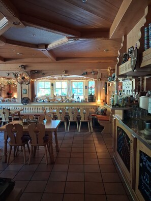 A restaurant with wooden furniture, a bar area, and a view through large windows.