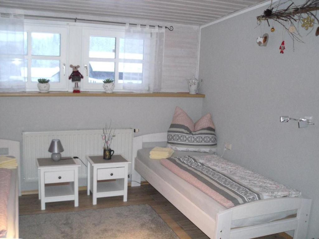 A bedroom with a bed, two bedside tables, a radiator, a window with curtains, and a shelf with decorative items.