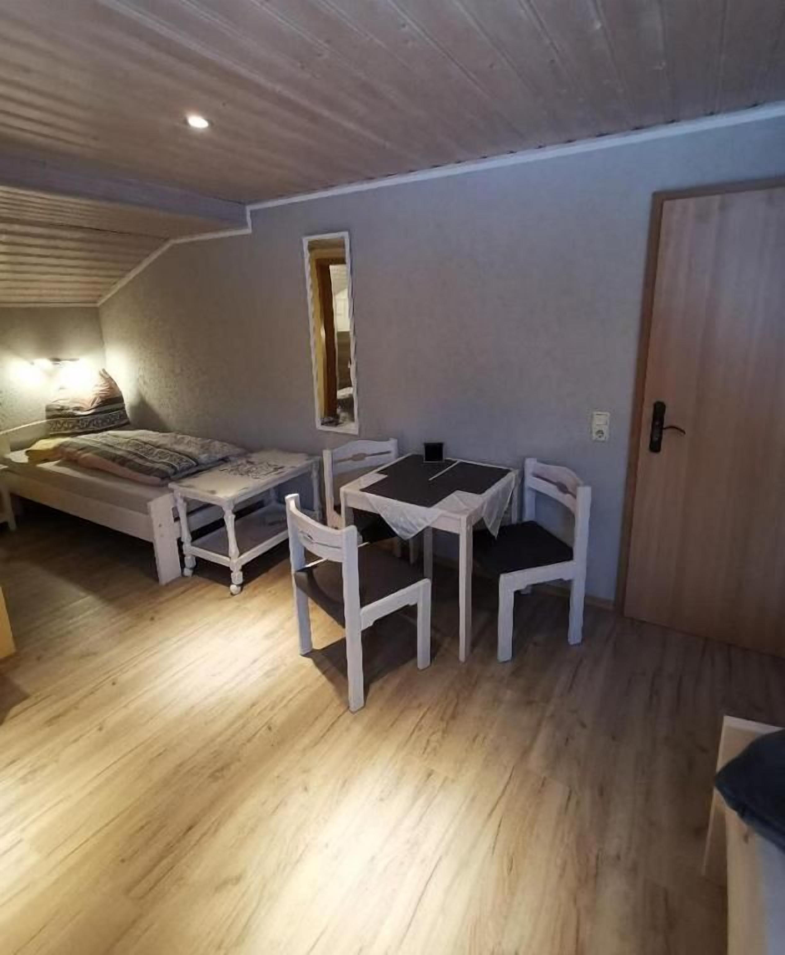 Een kleine kamer met een bed, een tafel met stoelen, een houten deur en een raam.