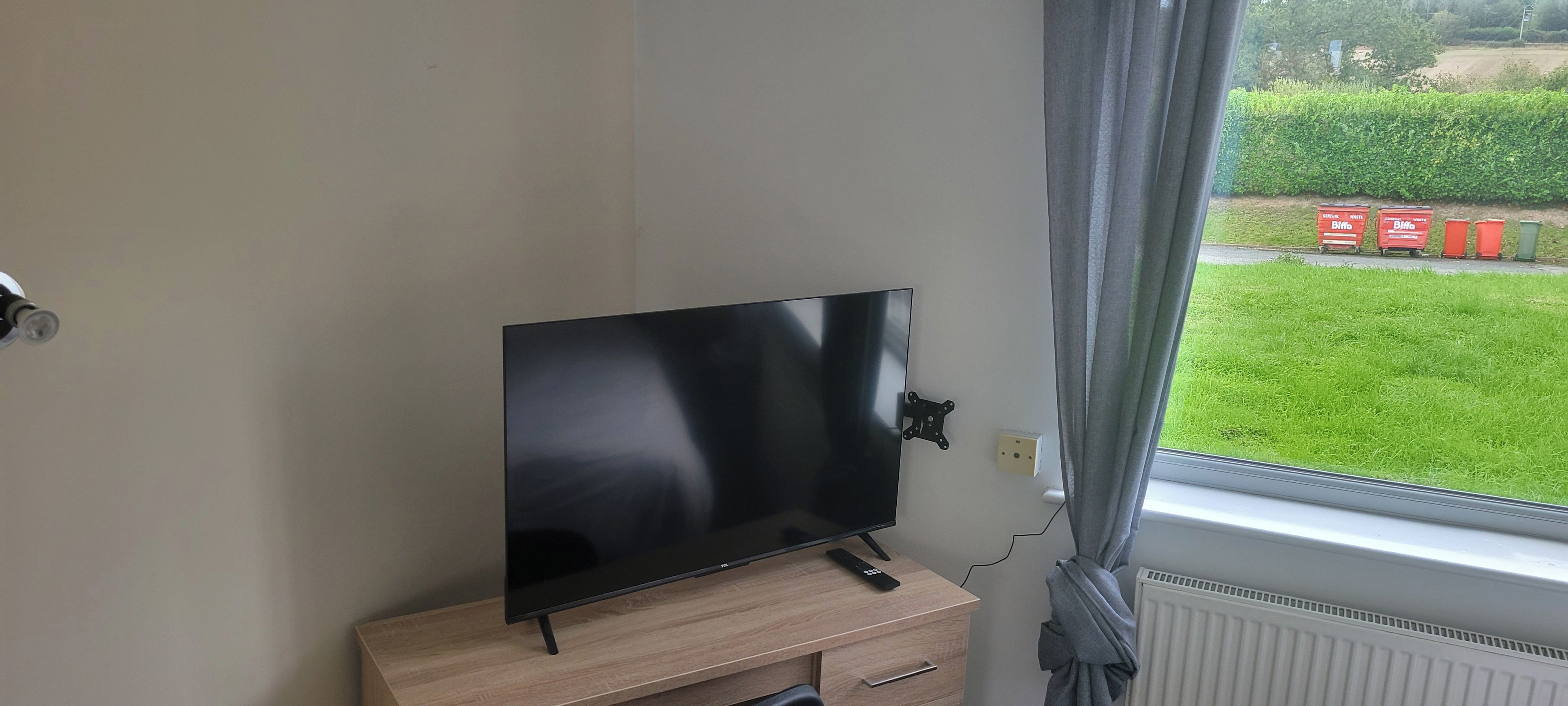 A flat-screen TV on a wooden stand in a room with a window.
