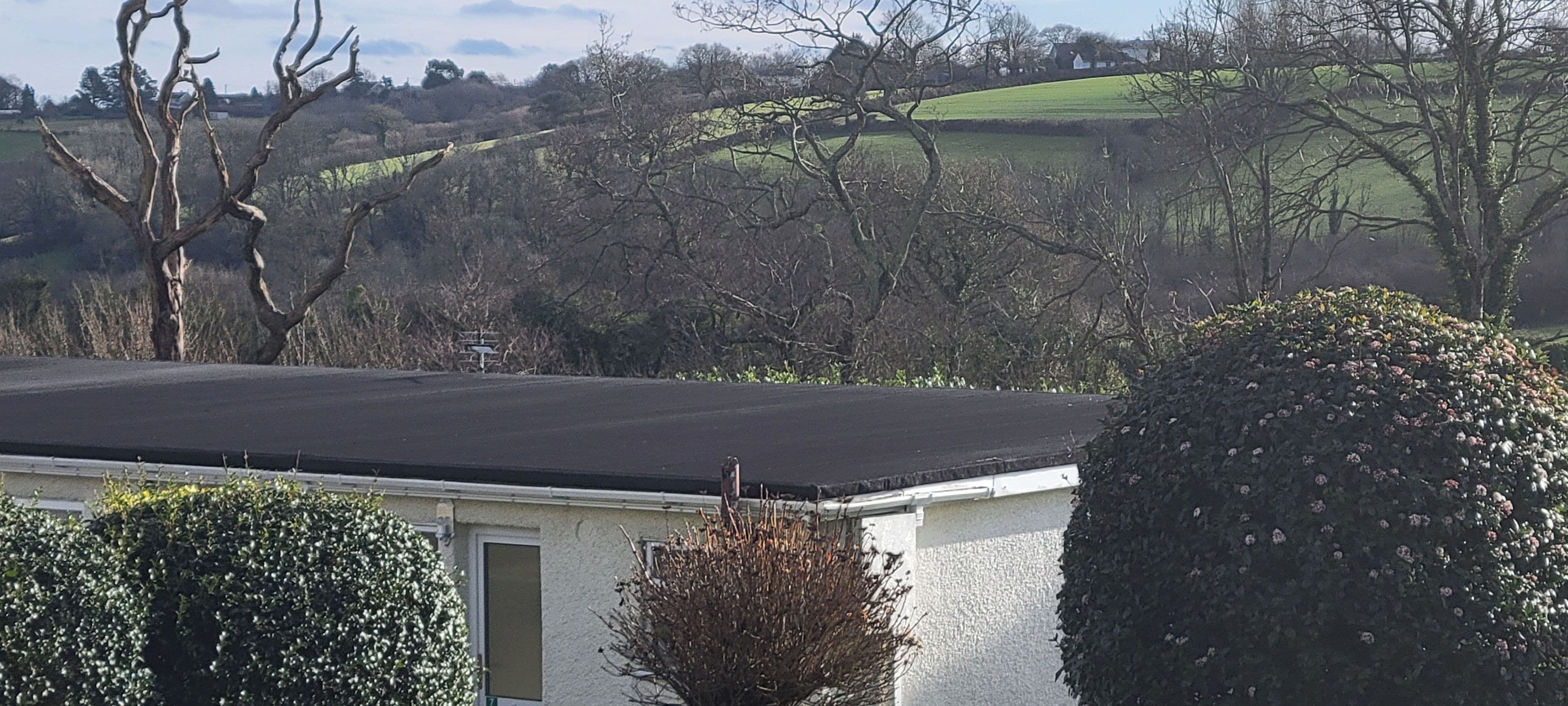 A building with a flat roof, surrounded by trees and a green field in the background.