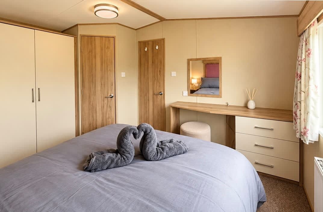 A bedroom with a bed, a wooden wardrobe, a desk with a mirror, and a window with curtains.