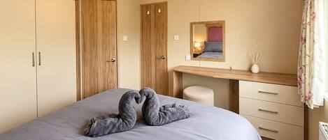 A bedroom with a bed, a wooden wardrobe, a desk with a mirror, and a window with curtains.