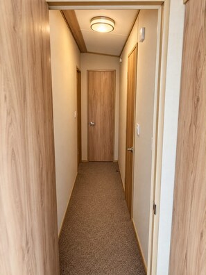 A narrow hallway with wooden walls and a carpeted floor, leading to a door at the end. - Thurston Manor Caravan - Sleeps 6 - Nr Power Station (Dunbar)