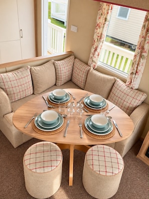 A round dining table with a beige sofa and matching ottomans, set with blue plates and silverware. - Thurston Manor Caravan - Sleeps 6 - Nr Power Station (Dunbar)