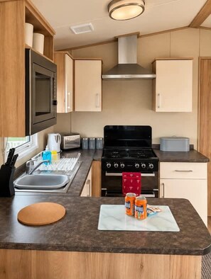 Une cuisine de taille réduite, équipée d’une cuisinière, d’un four à micro-ondes et de placards.