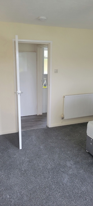 A room with a grey carpet, a white radiator, and a door leading to another room. - Apartment 27 Sleeps 2 With Enclosed Garden (Saltash)