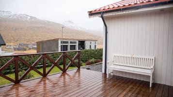Een houten terras met een witte bank, een metalen hekwerk en een gebouw met een rood dak.