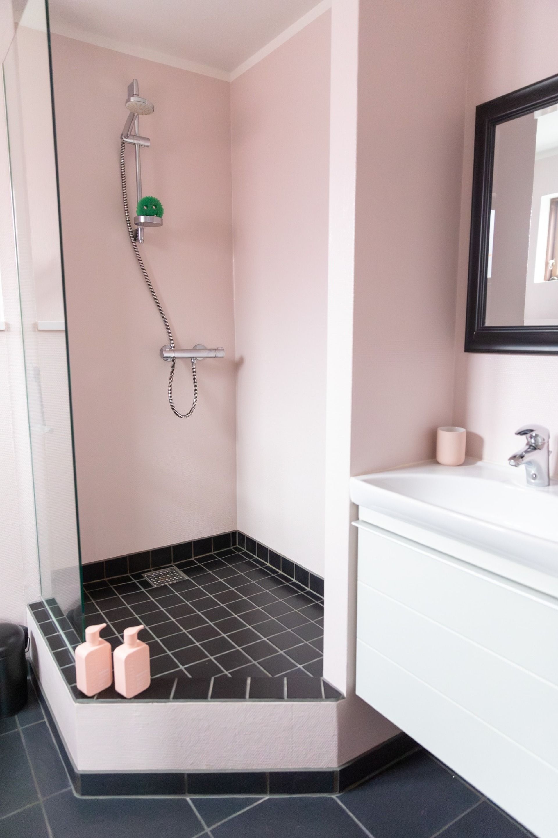 A modern bathroom with a glass shower enclosure, a white vanity, and a black tiled floor.