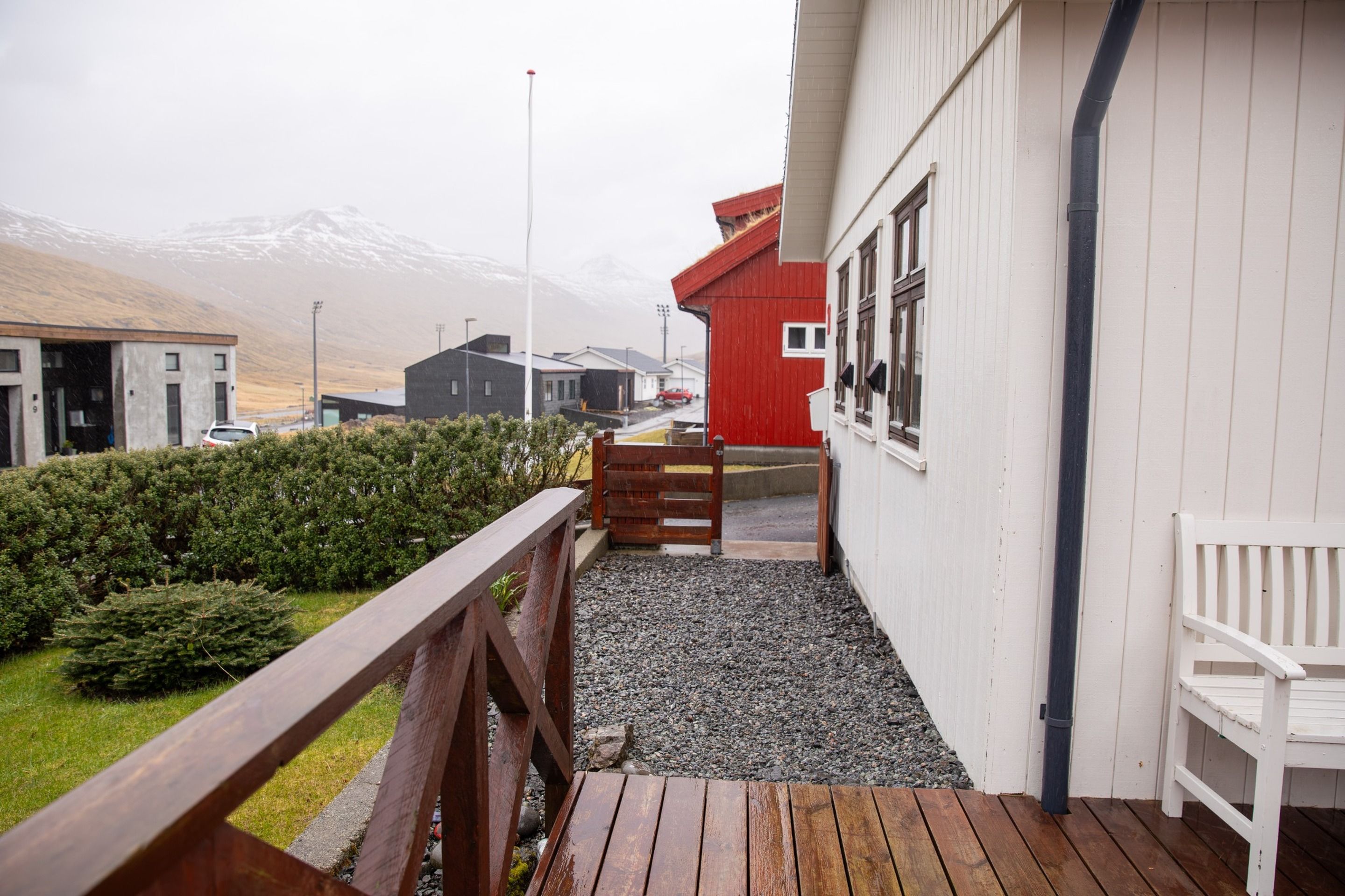 Una terraza de madera con un banco, un edificio rojo y una montaña al fondo.