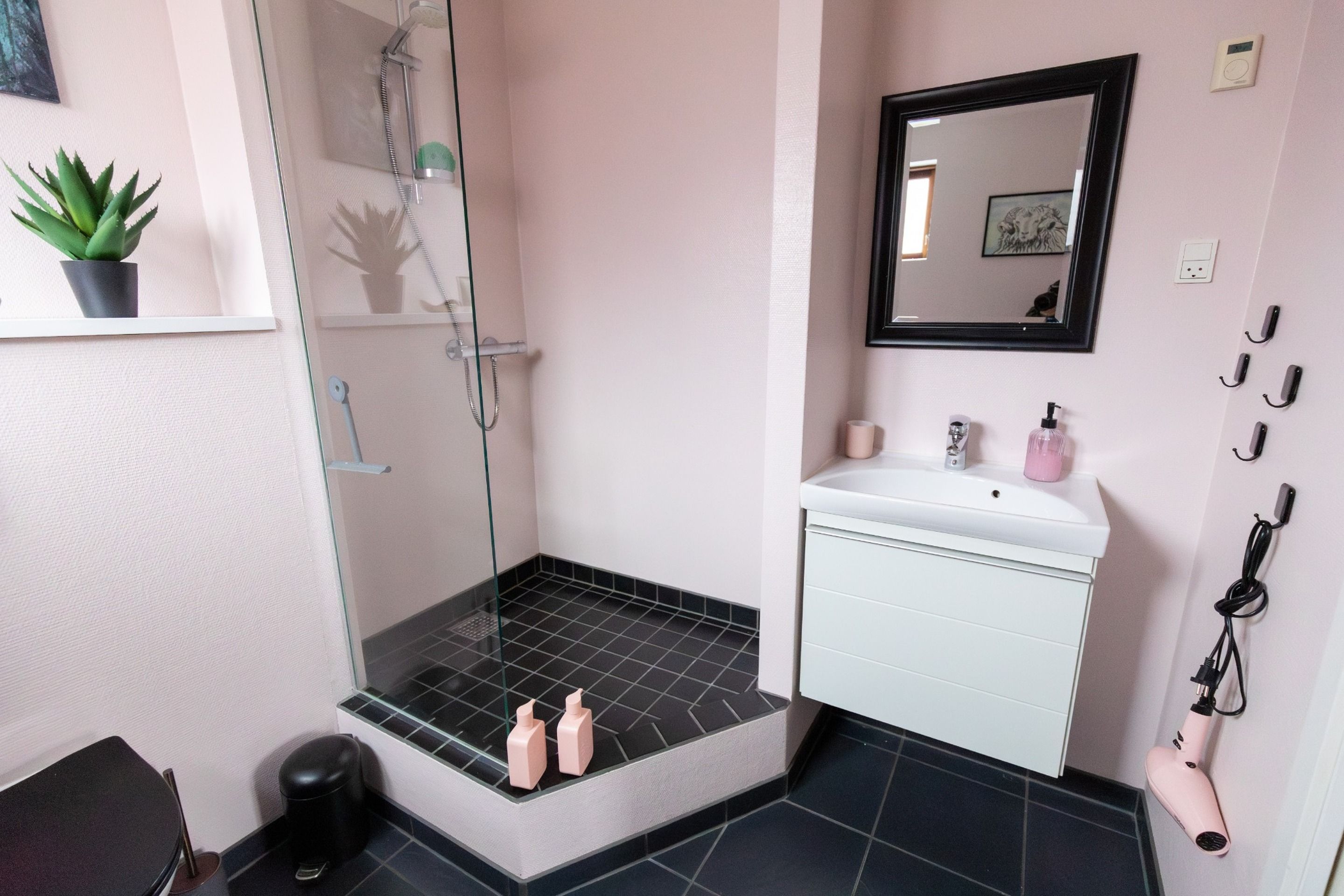 A bathroom with a glass shower enclosure, a white sink with a mirror above it, and a black tiled floor.