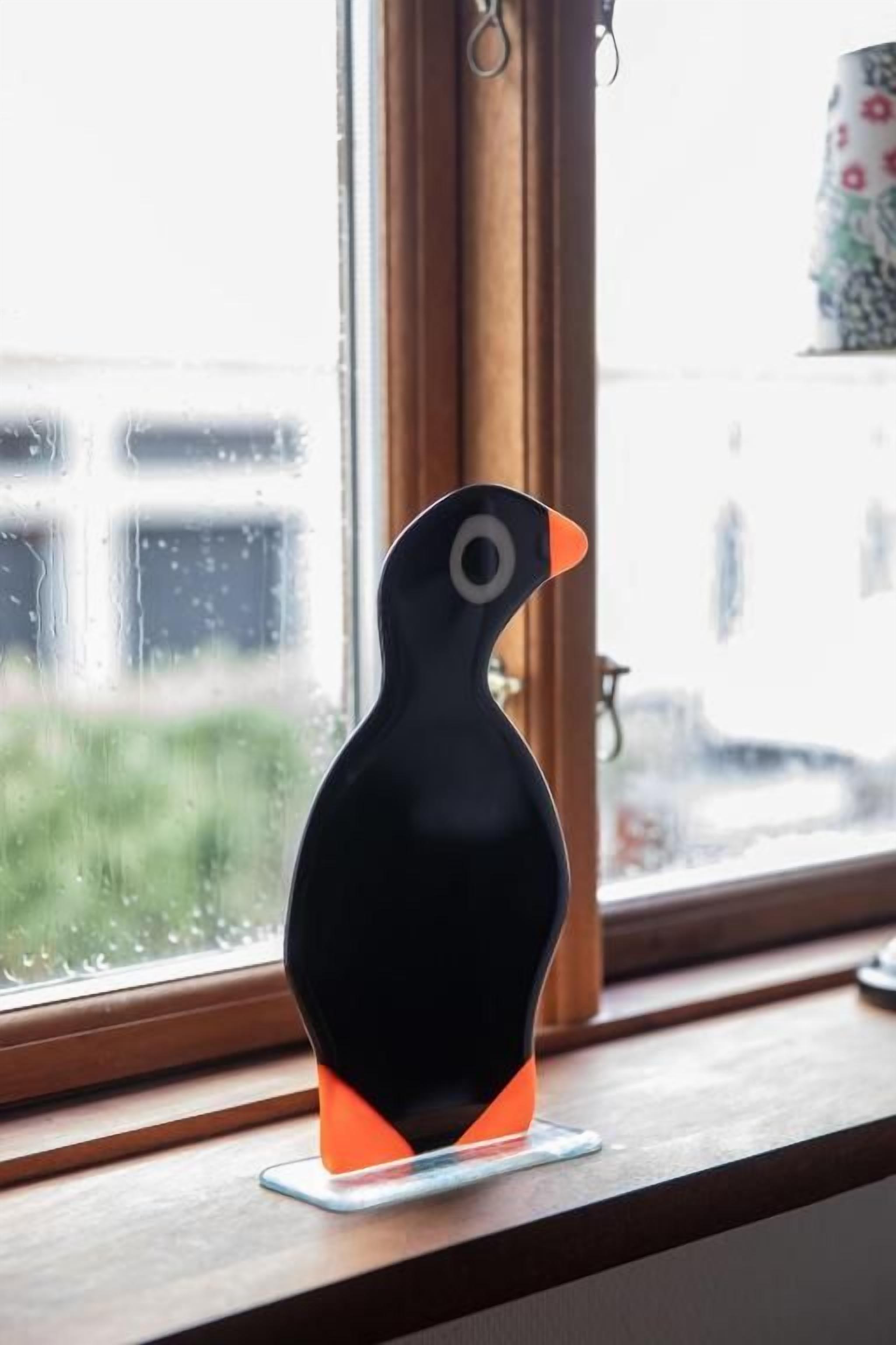 A black and orange penguin-shaped object on a clear glass surface near a window.