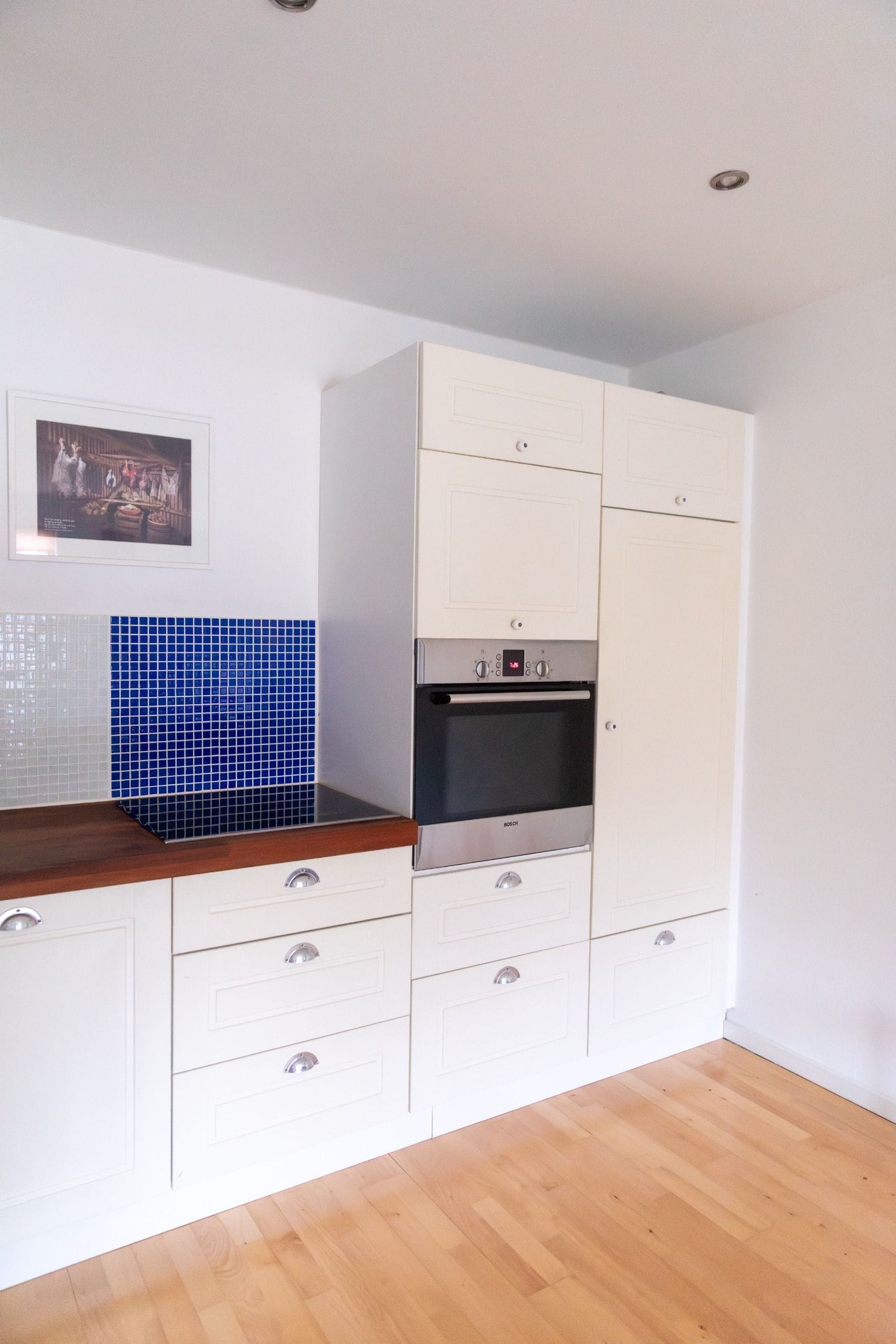 A kitchen with white cabinets, a Bosch oven, and a blue tiled backsplash.