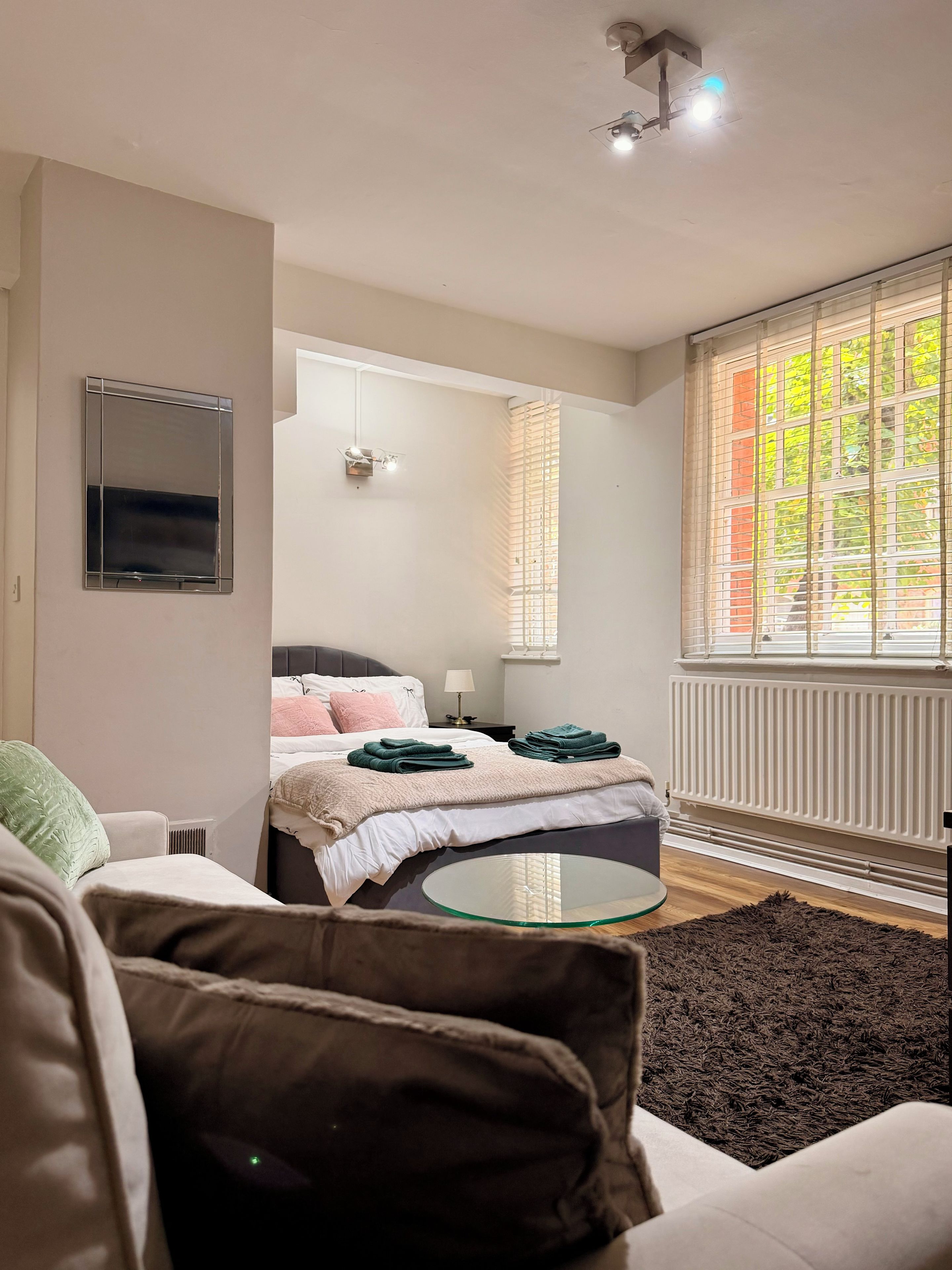 A modern bedroom with a bed, bedside table, lamp, and a view of the outdoors through a window.