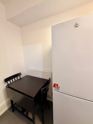 A small room with a white radiator, a dark wooden table with four chairs, and a white refrigerator. - Cosy London Stay near Shoreditch (London)