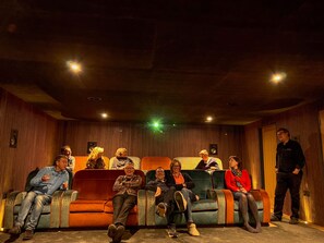 A group of people seated on a row of sofas in a dimly lit room with wooden paneling and recessed lighting. - Beautiful new build with outstanding views, huge lounge, high quality cinema. (Kirkby Stephen)