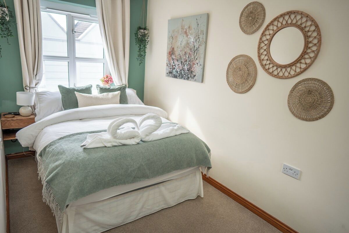 A bedroom with a bed, pillows, a bedside table with a lamp, a window with curtains, and wall decor.