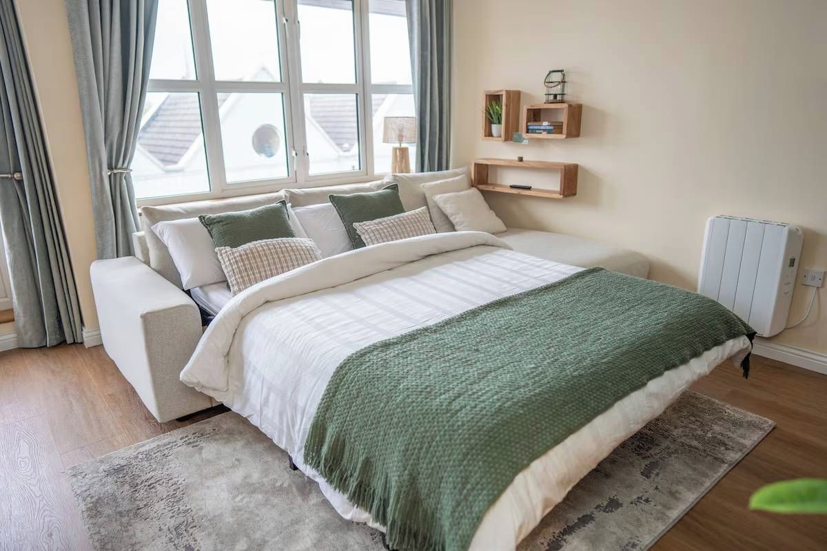 Une chambre à coucher avec un lit, des tables de chevet, un radiateur et une fenêtre avec des rideaux.
