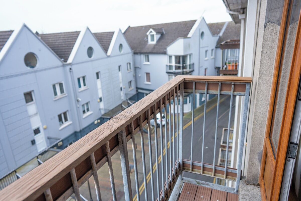 Ein Balkon mit Holzgeländer, der auf eine Straße mit Wohnhäusern blickt.