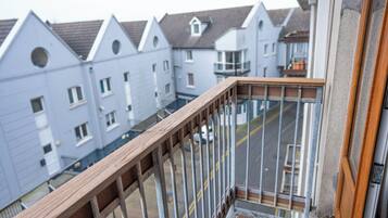Ein Balkon mit Holzgeländer, der auf eine Straße mit Wohnhäusern blickt.