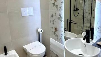 Une salle de bain comprenant des toilettes, un bidet, un lavabo et une douche.