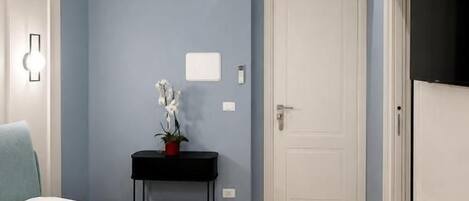 A hotel room with a bed, a bedside table with a lamp, a wall-mounted air conditioner, and a door.